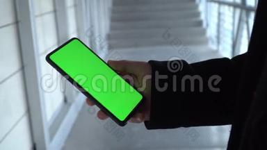 绿色屏幕智能手机。 一个男人`手拿着电话。 在手机的绿色屏幕上滚动。 智能手机录像。